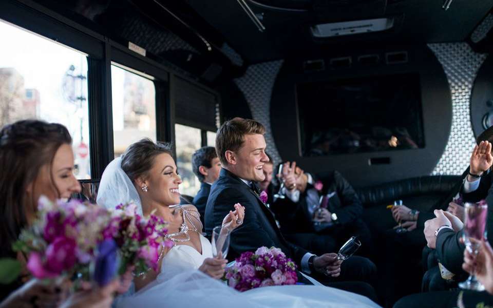 Bride, groom and wedding party toasting with champagne inside a party bus