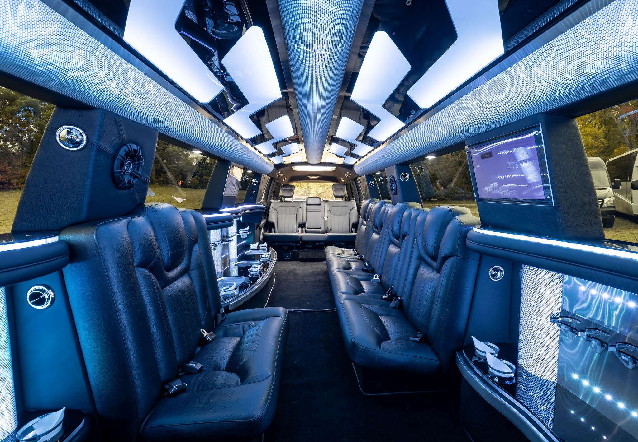 Stretch limo interior with black leather bench seats, lit ceiling panels and a TV screen