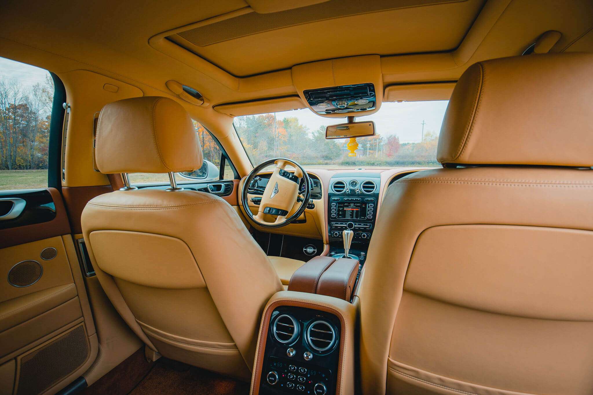 Bentley interior with tan leather seats, wood trim and dashboard, seen from the back seat