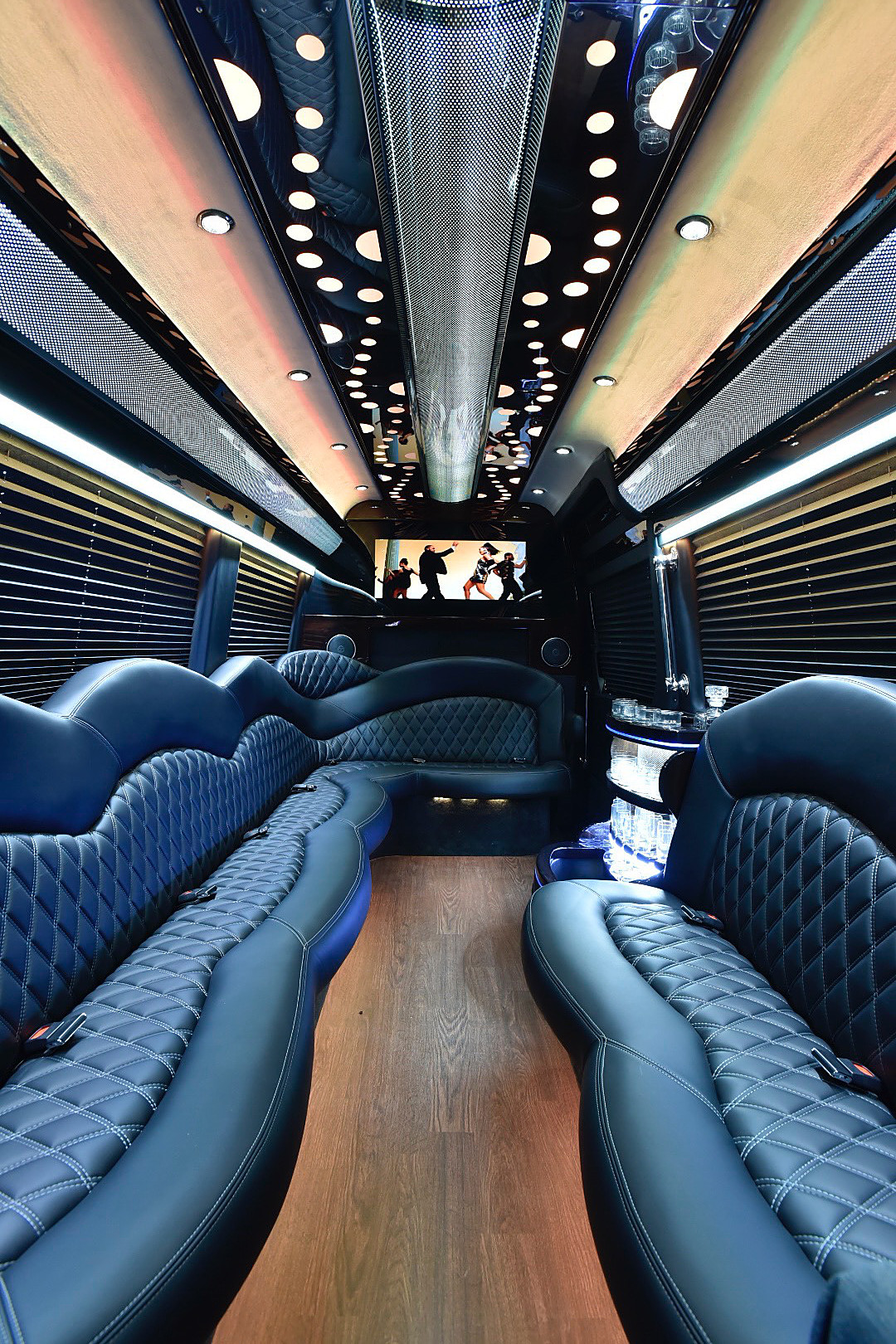 Limo van interior with dark blue quilted leather seats, wood-look floor, bar and TV