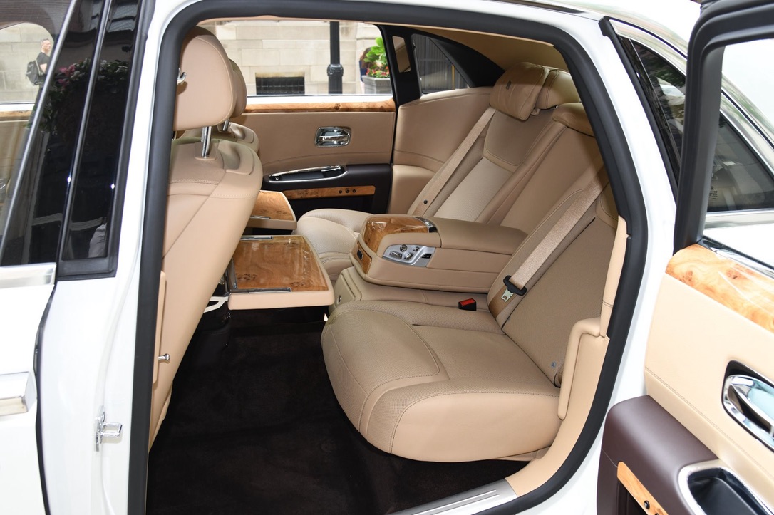 Cream leather rear seats and wood picnic tables inside a white car, door open