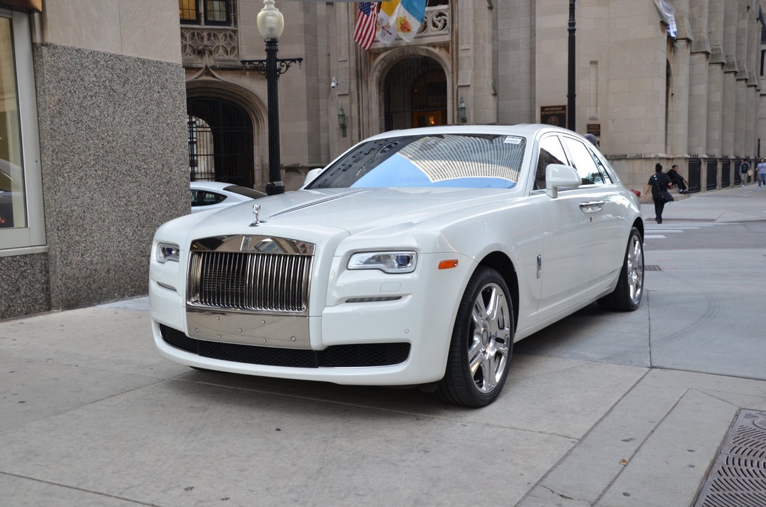 White Rolls-Royce Ghost parked on a city sidewalk beside a stone building