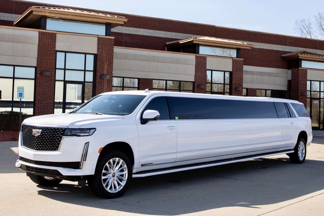 White stretch Cadillac Escalade limousine parked outside a brick building