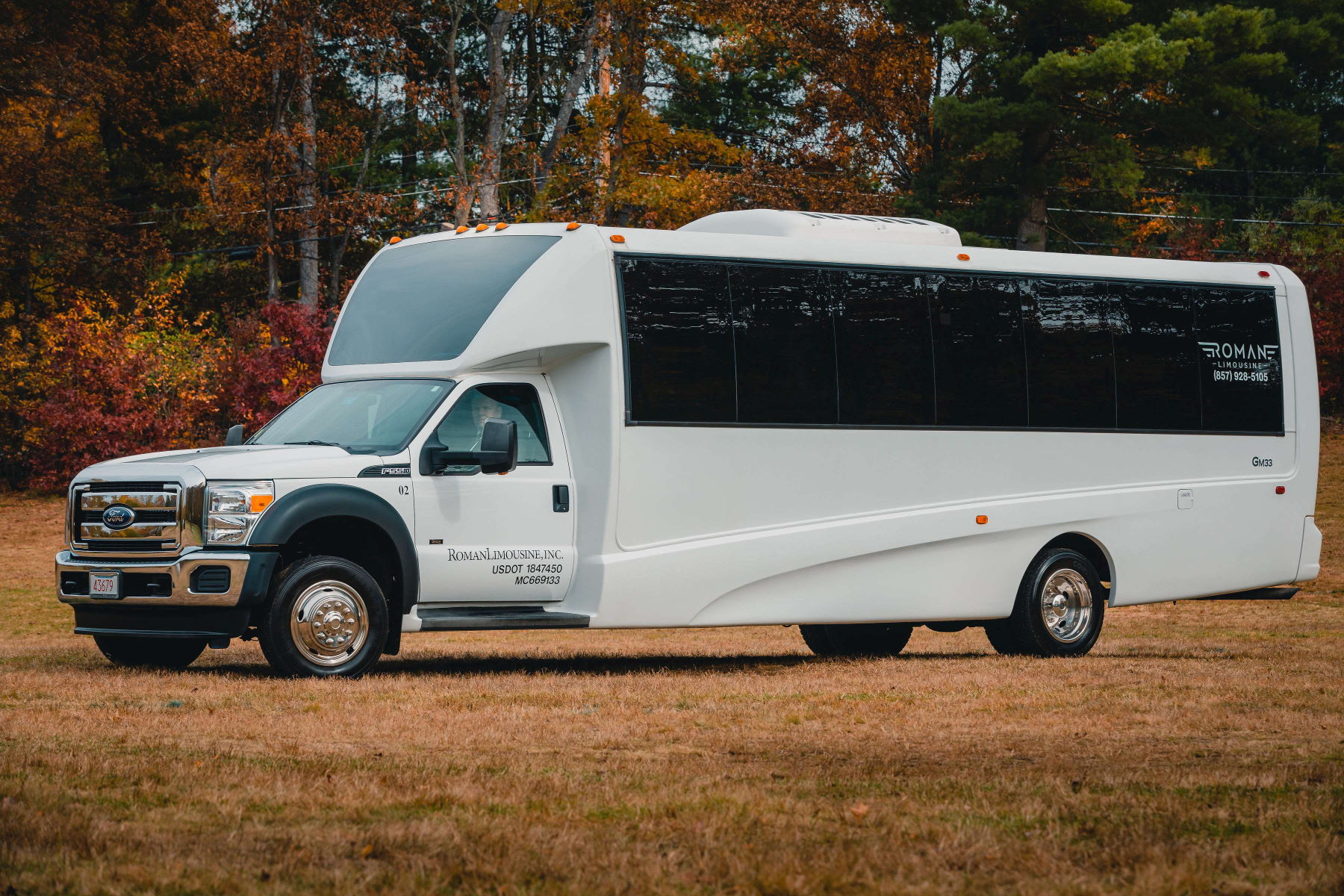 White Roman Limousine party bus with tinted windows parked on grass in autumn