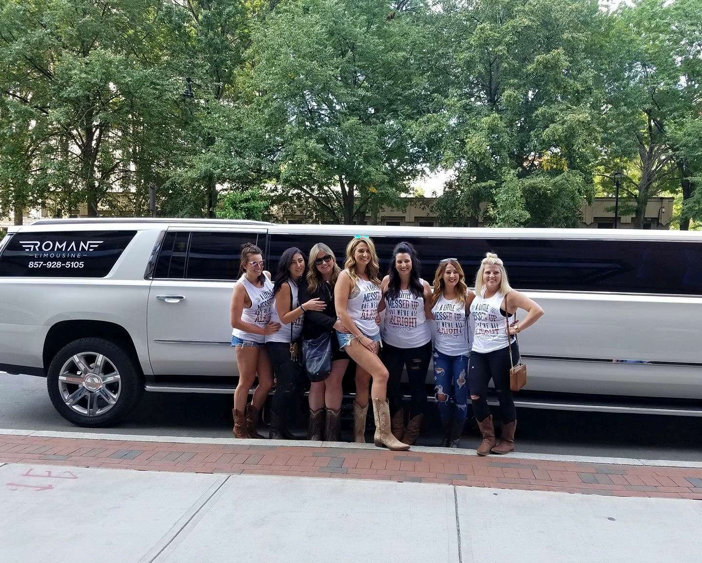 Bachelorette group in matching tank tops posing beside a white Roman Limousine stretch SUV