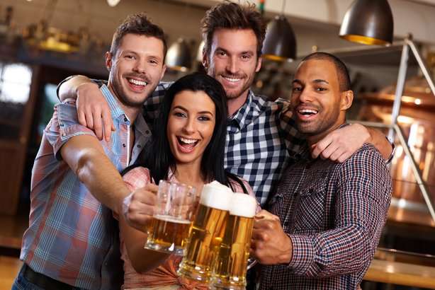 Four friends smiling and raising mugs of beer in a bar