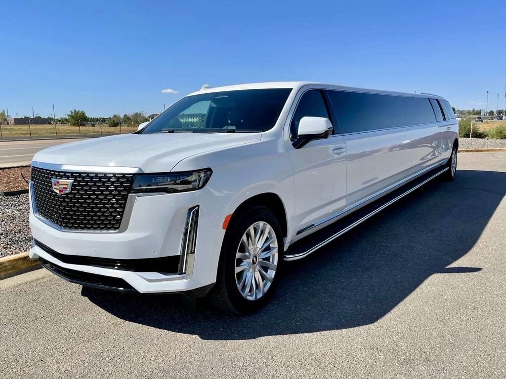 White Cadillac Escalade stretch limousine parked in an empty lot under a blue sky