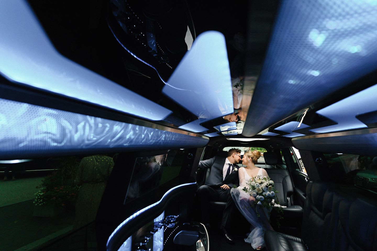 Bride and groom kissing in the back of a limousine under a lit ceiling