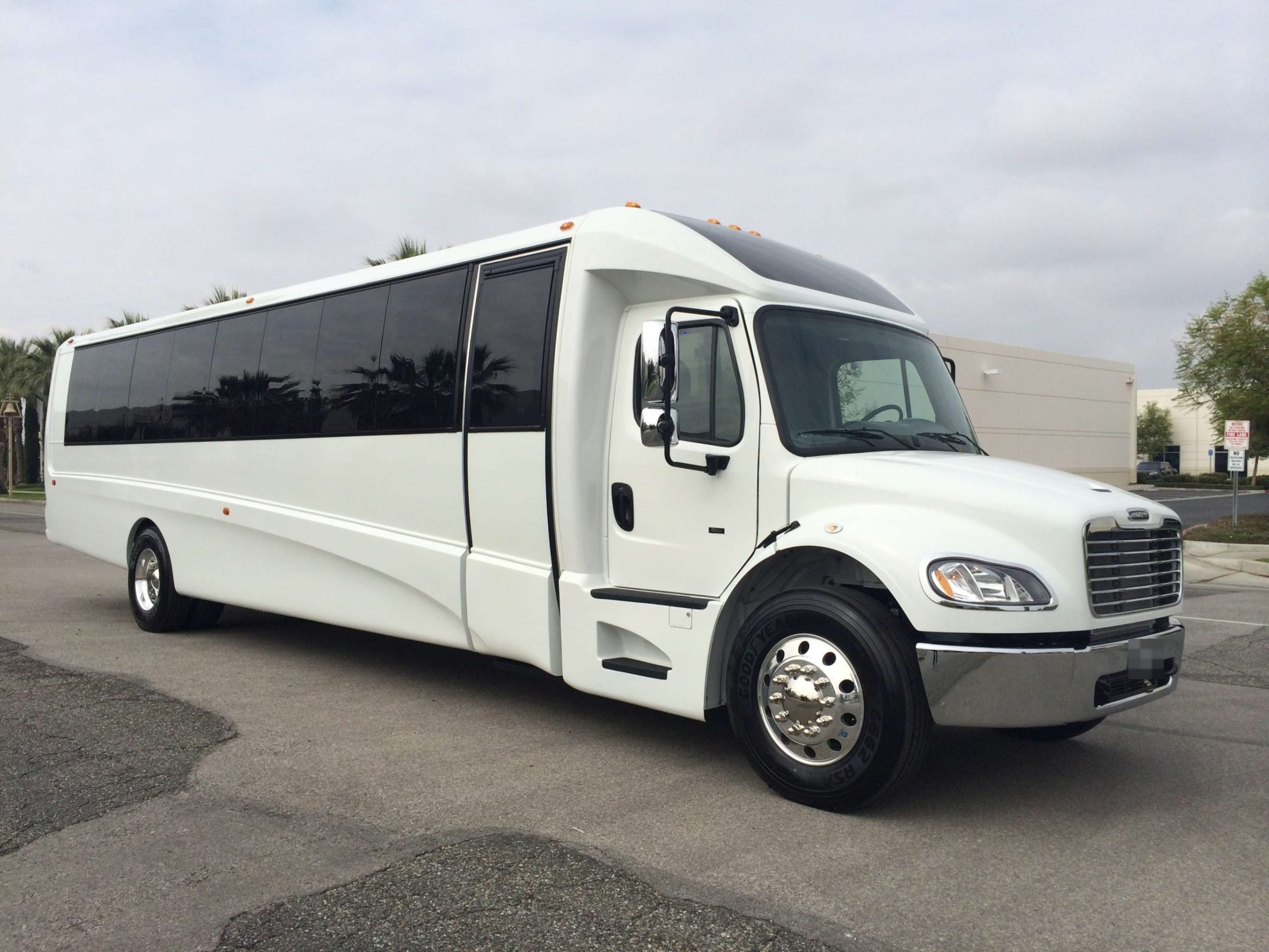 White party bus with tinted windows parked in a lot under a cloudy sky