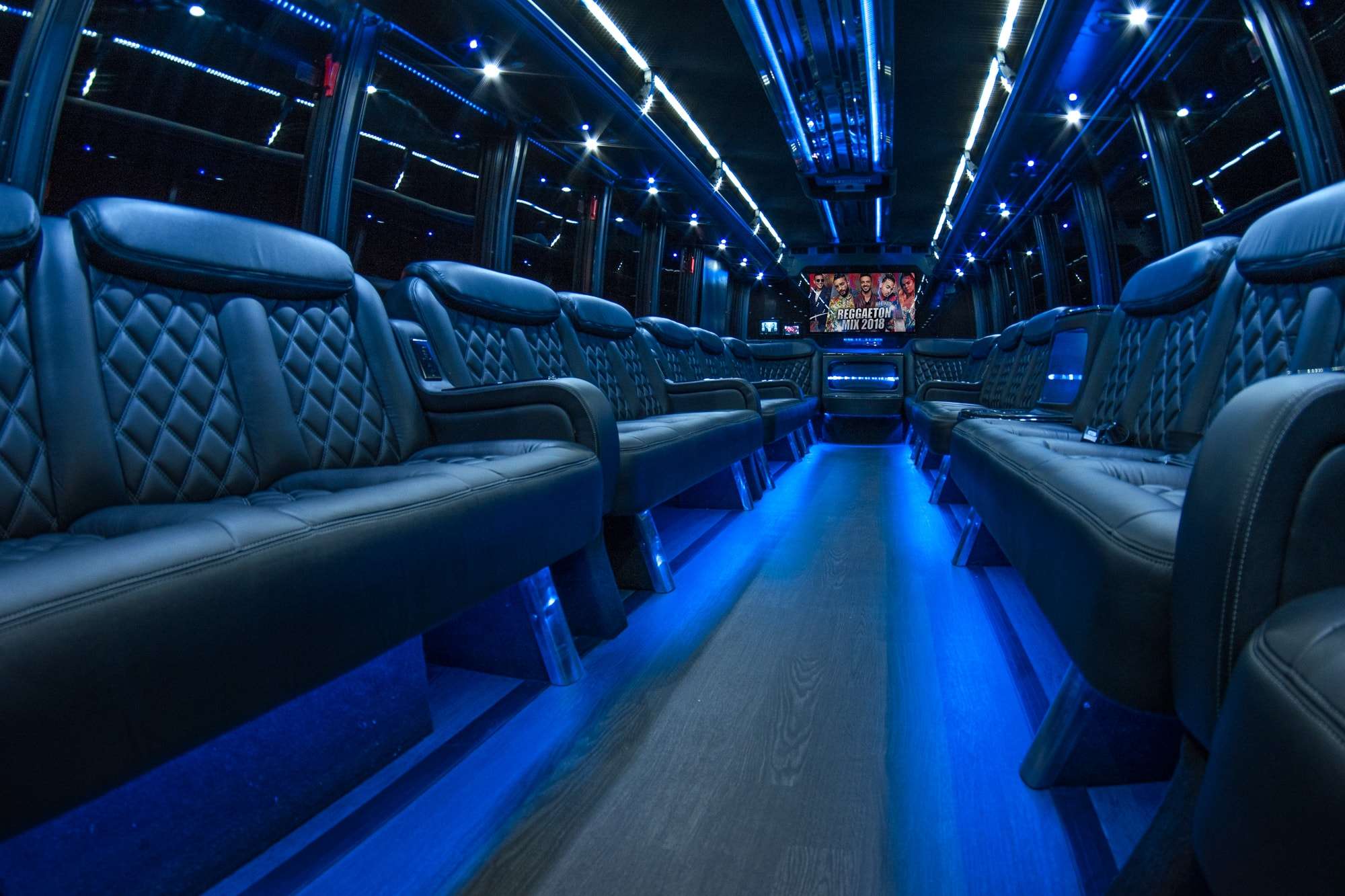 Party bus interior with quilted black leather side seats, blue floor lights and a TV