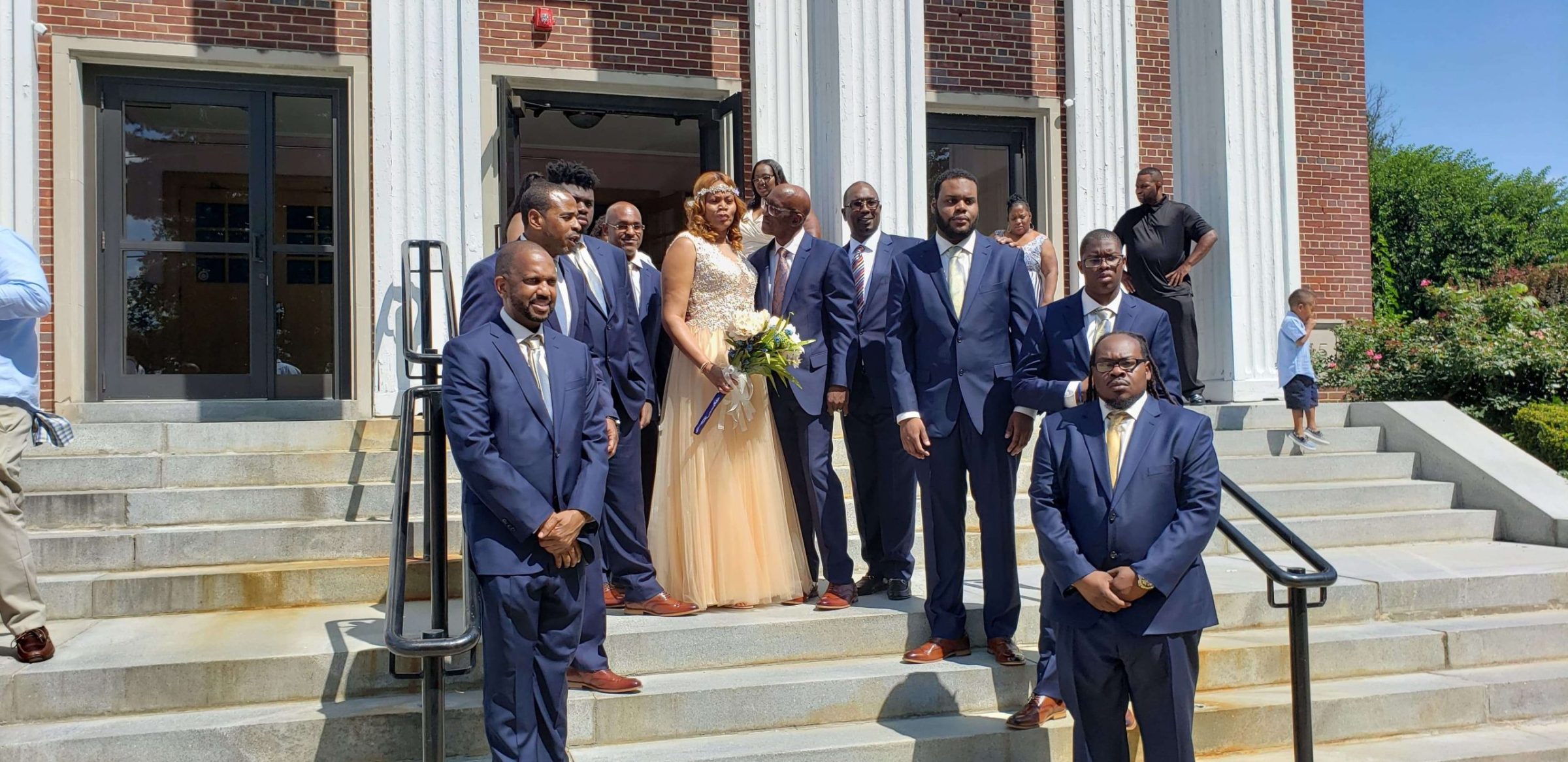 Bride in a gold gown with groomsmen in navy suits on building steps