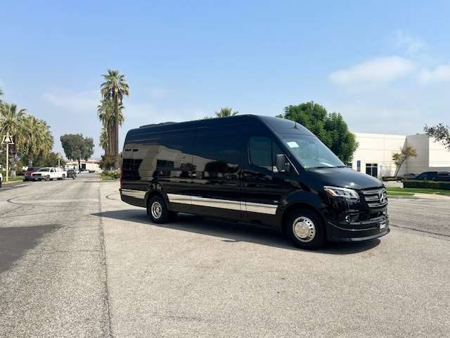 Black Mercedes-Benz Sprinter van with tinted windows on a sunny street with palm trees
