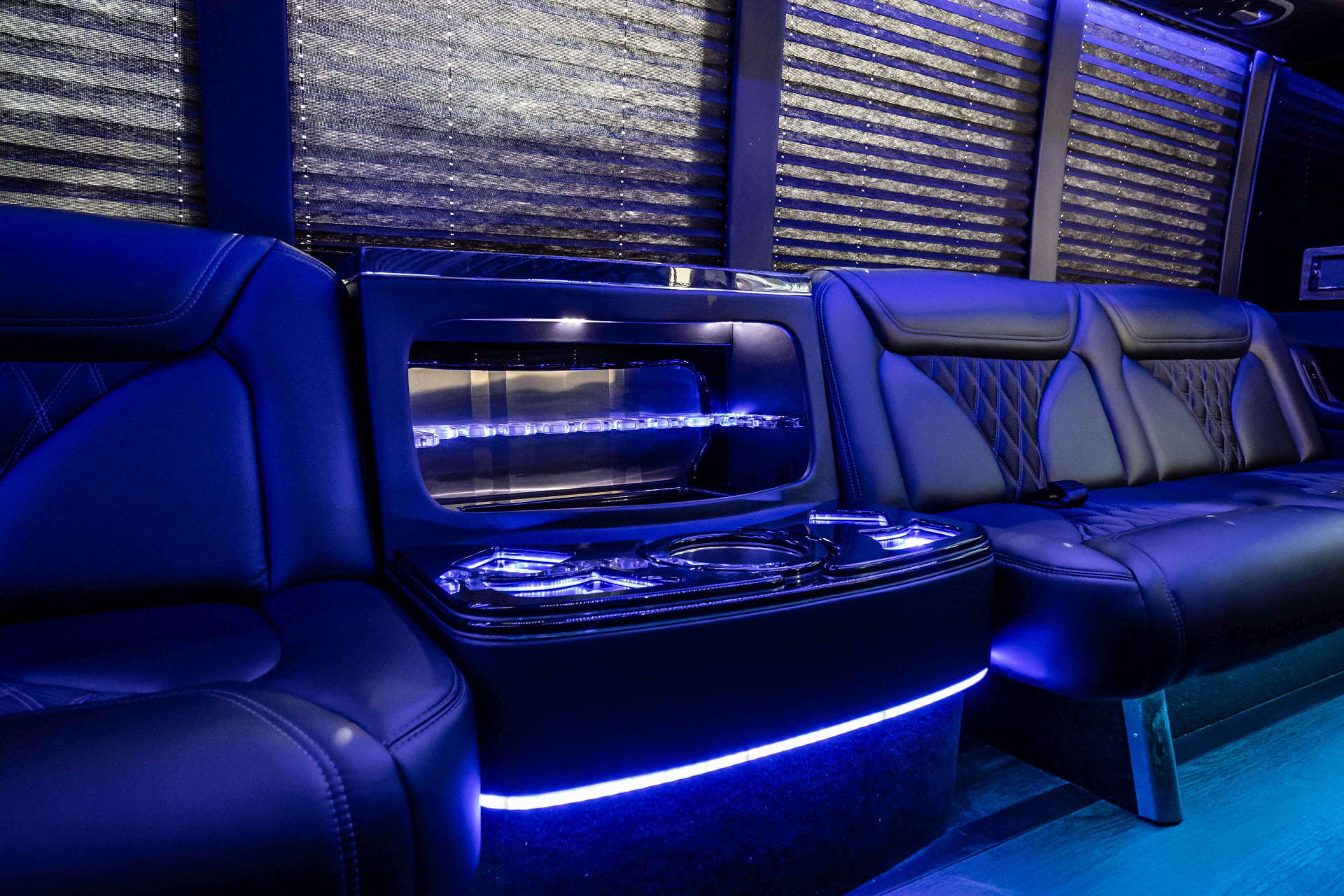 Party bus black leather seats beside a lit bar cabinet with cup holders