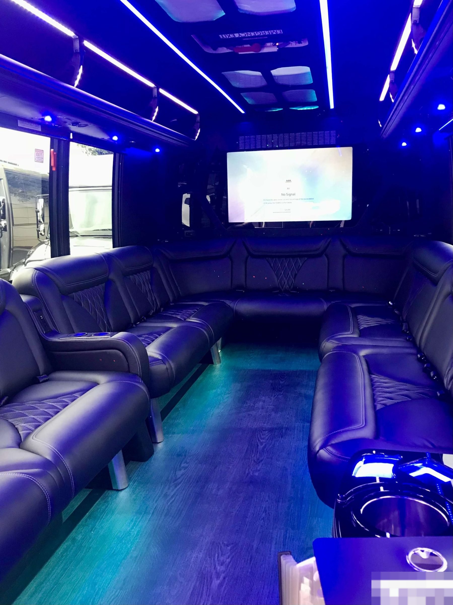 Limo bus interior with black leather wraparound seats, blue lights and a large TV