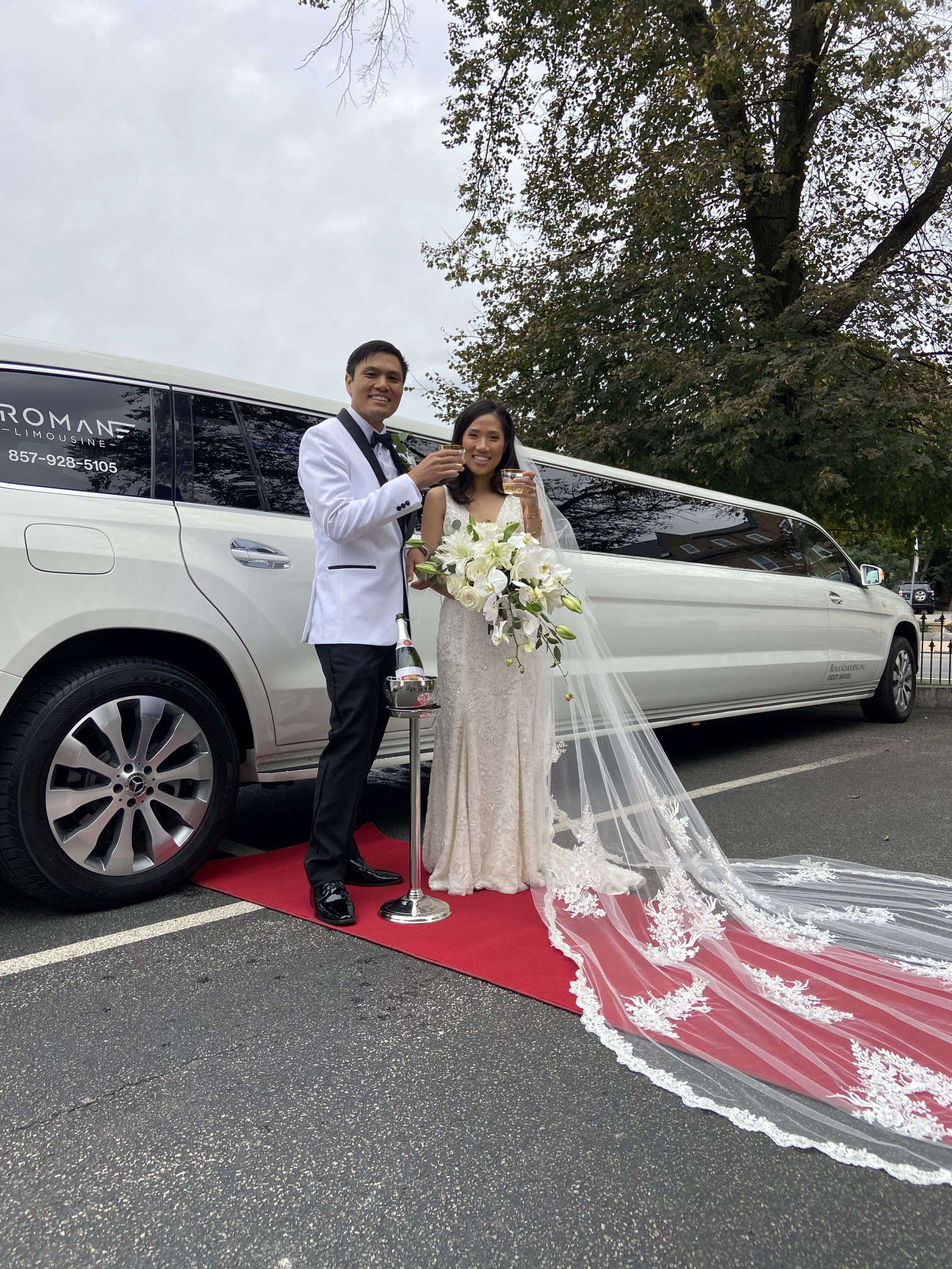 Bride and groom toasting on a red carpet beside a white stretch Mercedes-Benz SUV limousine