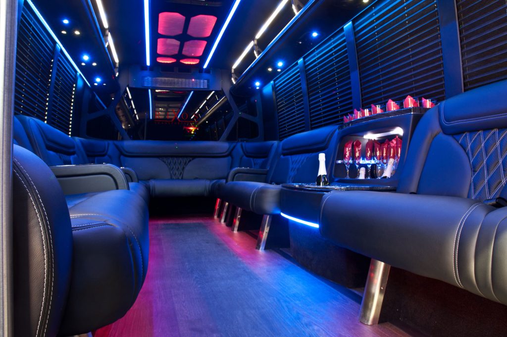 Limo bus interior with black leather seats, blue and pink lights and a champagne bar