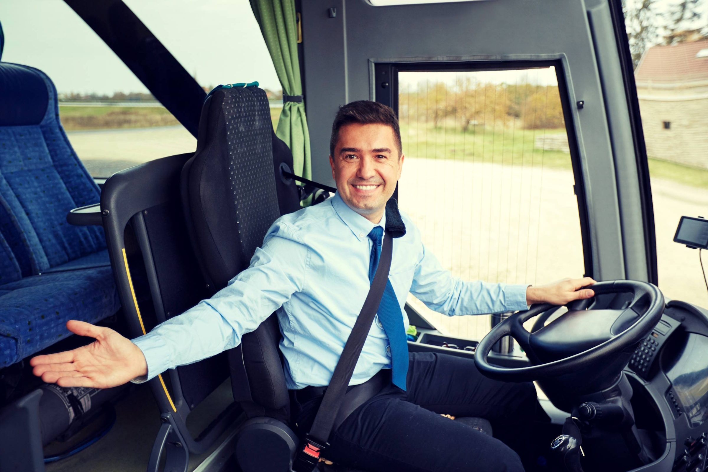 Smiling bus driver in shirt and tie at the wheel, gesturing to the seats