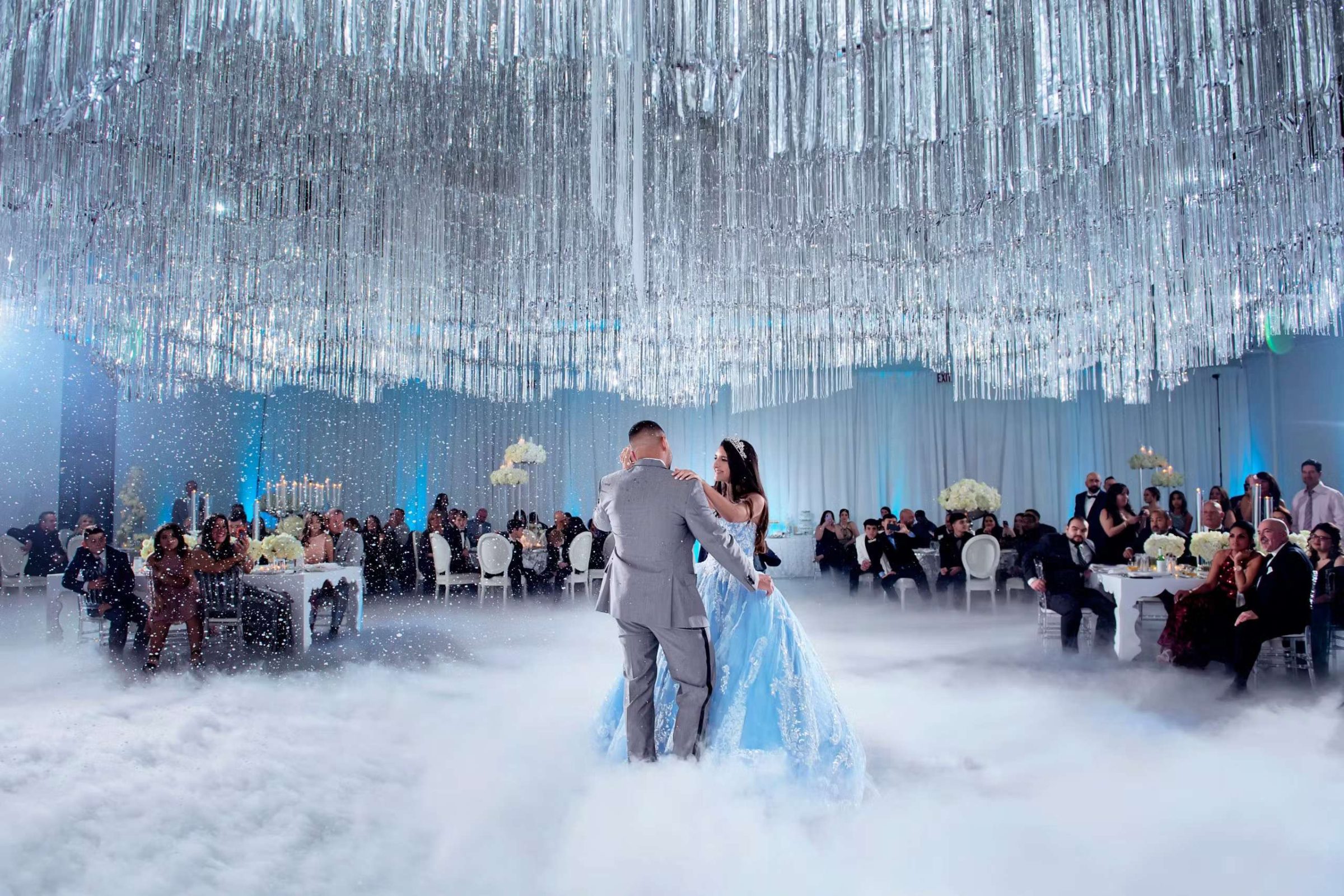 Girl in blue ball gown and tiara dancing with a man on a fog-covered floor
