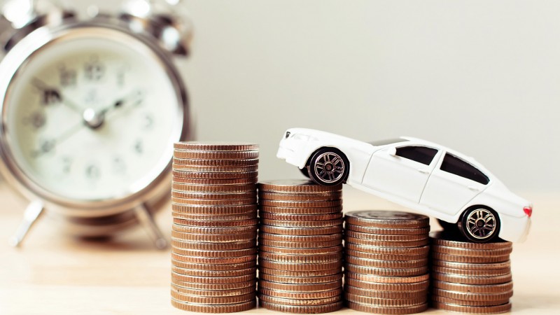 Toy car on rising stacks of coins next to an alarm clock