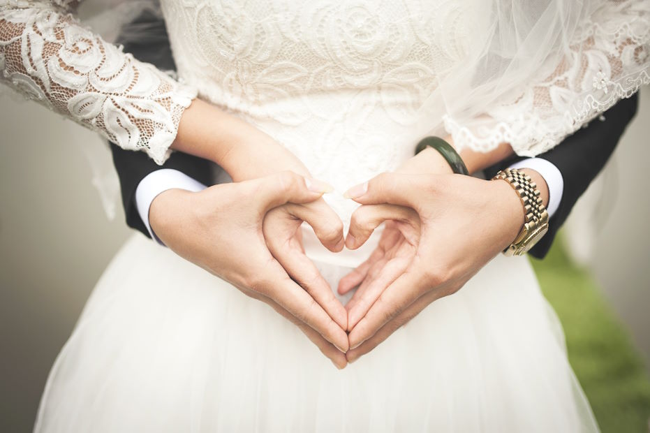 Bride and groom making a heart shape with their hands over a lace wedding dress