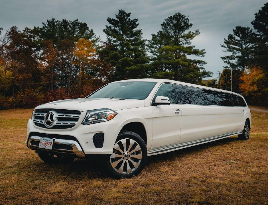 White Mercedes-Benz SUV stretch limousine parked on grass with autumn trees behind
