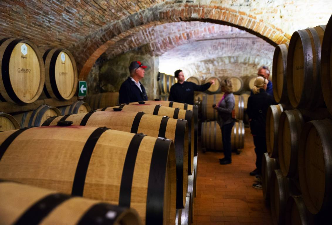 Visitors on a guided tour of a brick-vaulted wine cellar lined with oak barrels