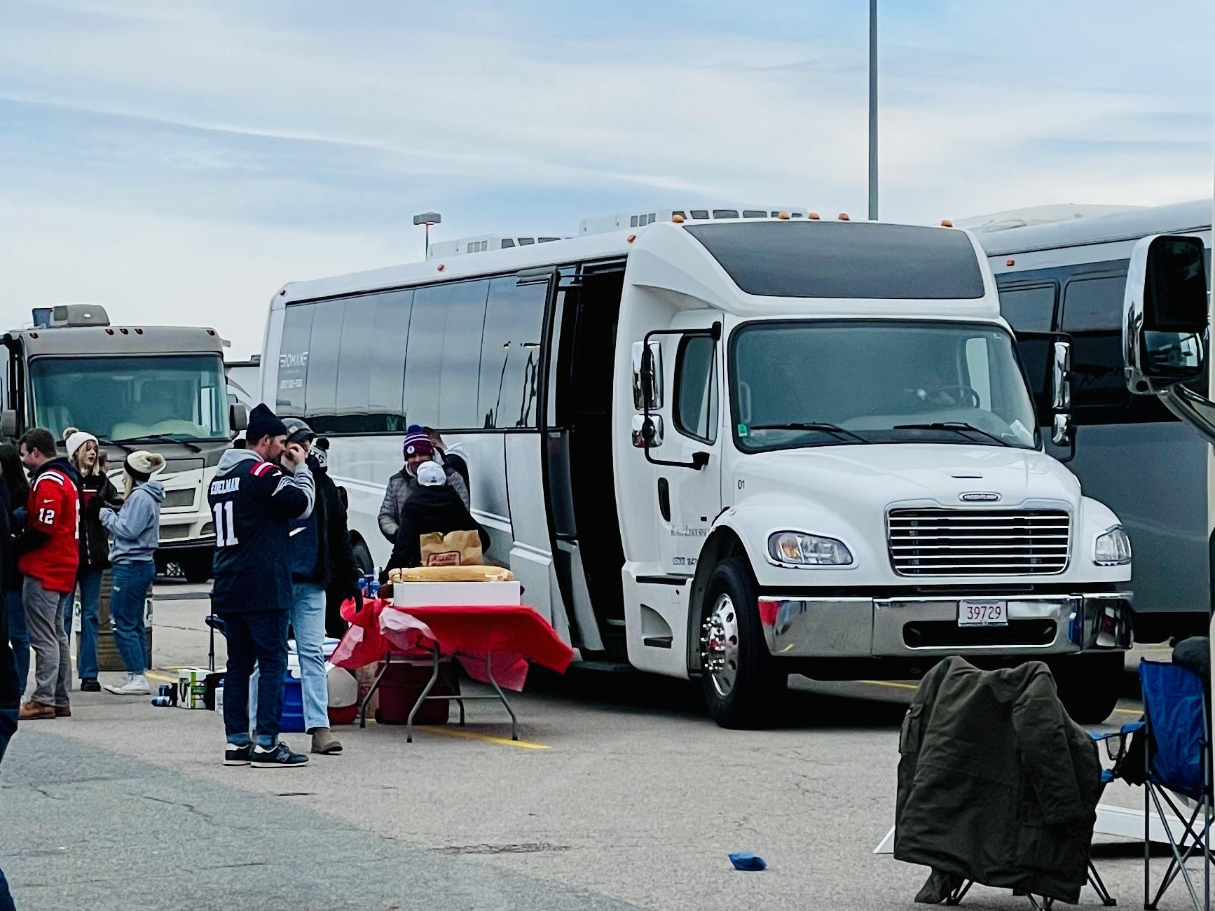 Football fans tailgating beside a white party bus in a stadium parking lot