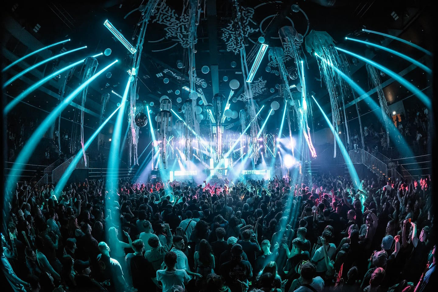 Crowd dancing under blue light beams at an indoor electronic music show