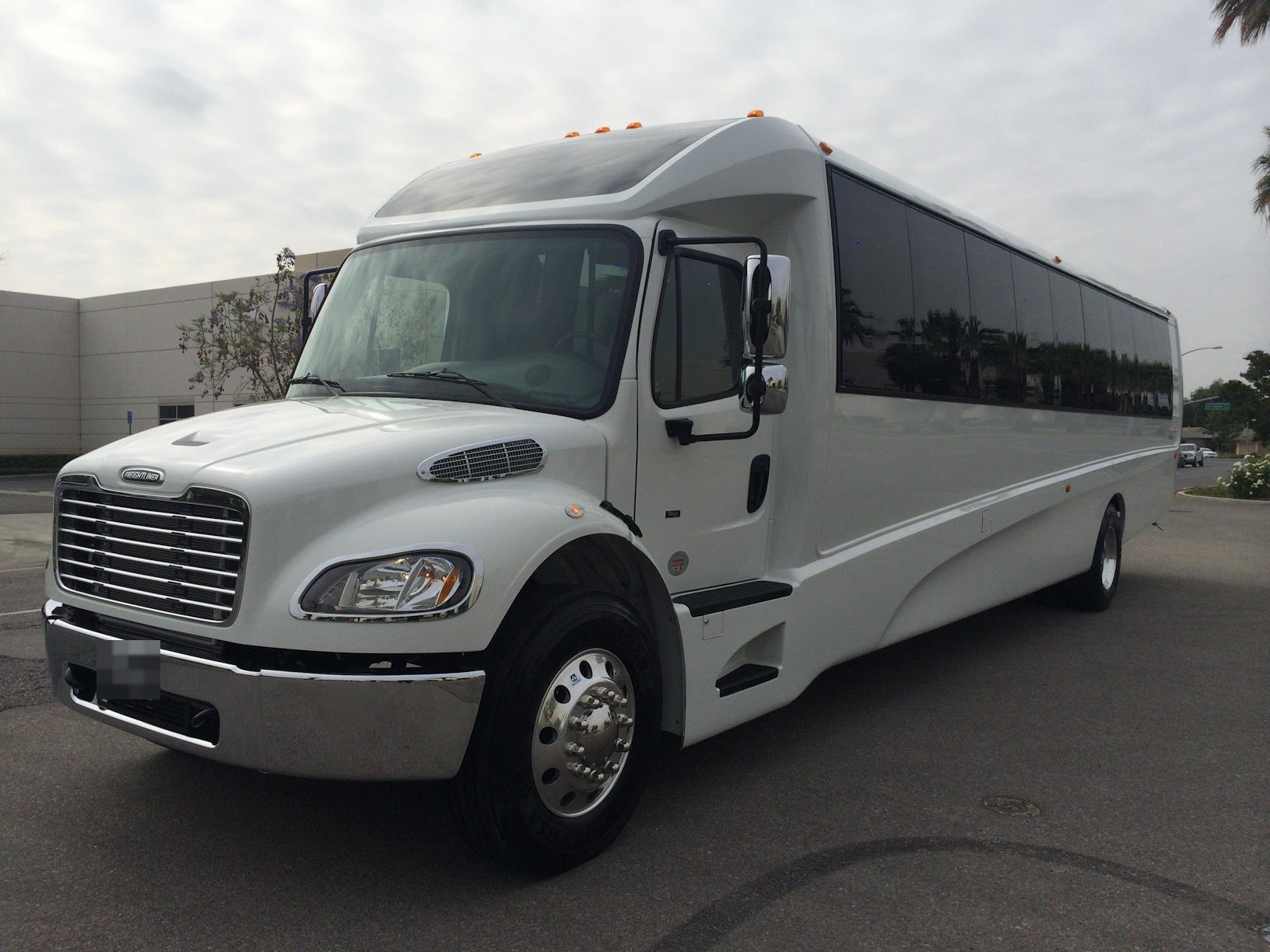 White party bus with tinted windows, front view, in a parking lot
