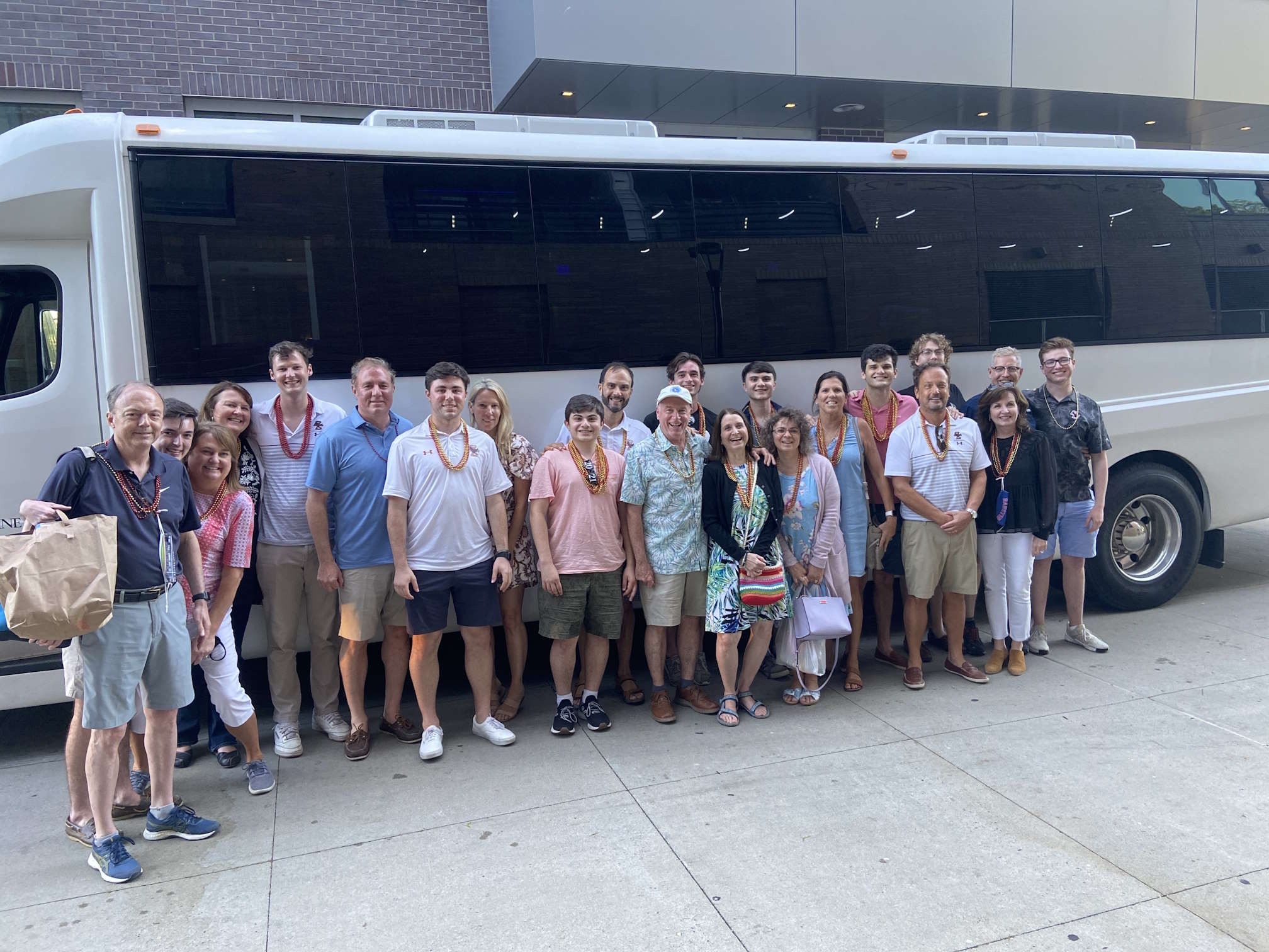Large group wearing leis posing in front of a white party bus on a sidewalk