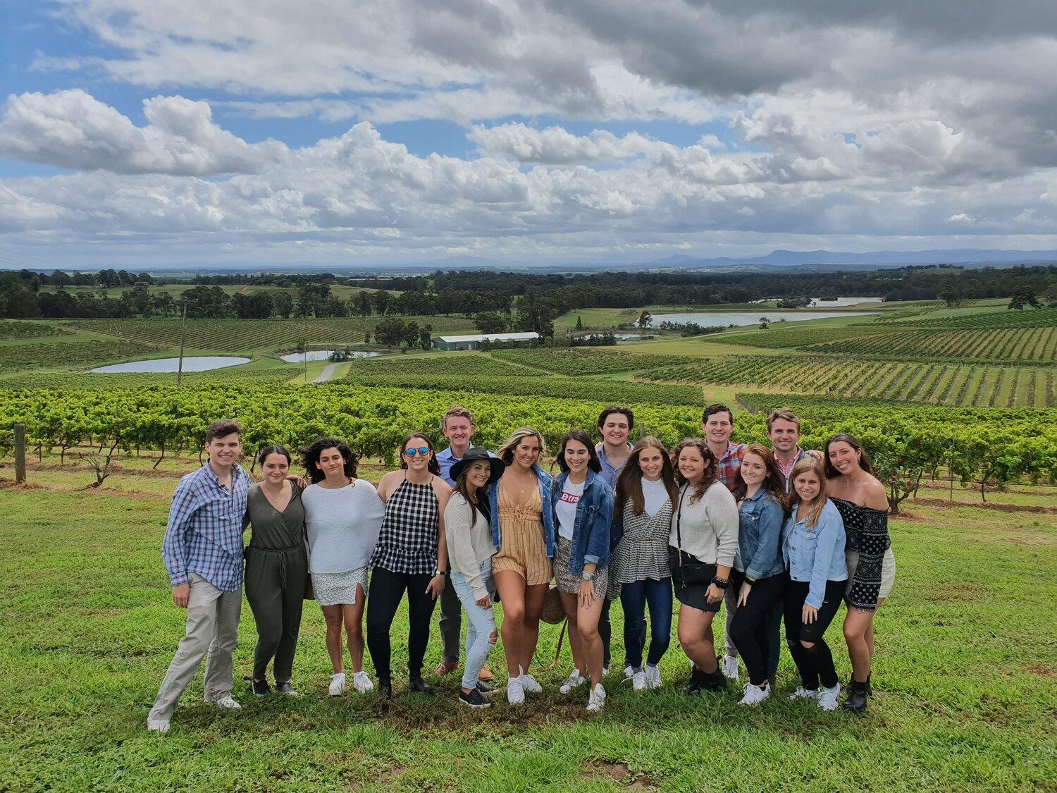 Group of young friends posing on a lawn in front of vineyard rows
